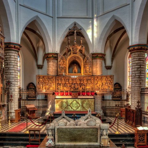 Prächtiges Kircheninnere mit hohen Bögen, bunten Glasfenstern und einem reich dekorierten Altar. Warmes Licht erzeugt eine ruhige und ehrfürchtige Atmosphäre.