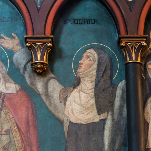 Ein Wandgemälde zeigt drei Nonnen in gemalten Bögen. Die zentrale Nonne gestikuliert leidenschaftlich nach oben. Die Szene vermittelt Hingabe und Ehrfurcht, hervorgehoben durch lebendige Farben.