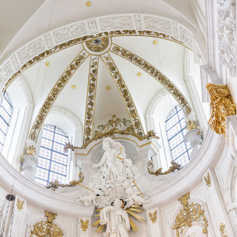 Ornate white and gold Baroque church interior with a domed ceiling, intricate sculptures, and large arched windows, conveying opulence and grandeur.