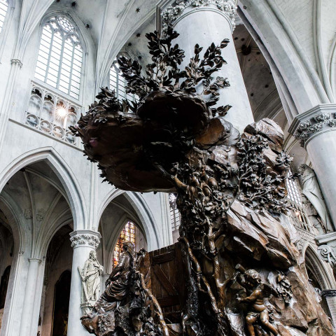 Gothic cathedral interior with towering white arches, large stained glass windows, and a detailed bronze sculpture, creating an awe-inspiring and solemn atmosphere.