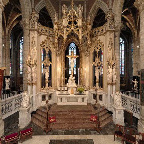 Prächtiges Kircheninnere mit einem großen Altar, der ein Kreuz und Statuen zeigt, umgeben von filigranen gotischen Bögen und bunten Glasfenstern.