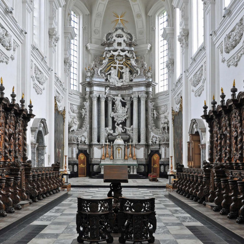 Prunkvolles barockes Kircheninnere mit kunstvollen Holzgestühlen und einem reichen Altar mit Skulpturen. Hohe Gewölbedecken und große Säulen verstärken die Pracht.