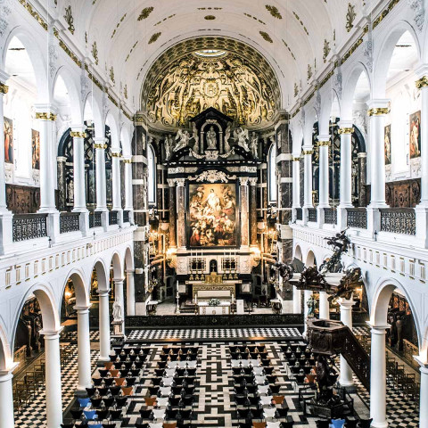 Innenraum einer großen Kirche mit schwarz-weiß kariertem Boden und kunstvoller Architektur. Hohe gewölbte Decken, aufwändiger Altar; düstere, aber beeindruckende Atmosphäre.