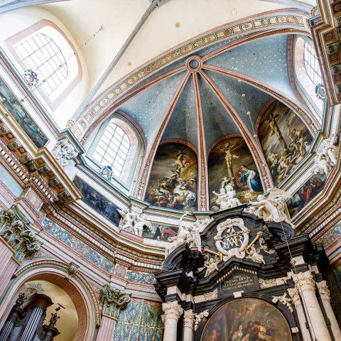 An ornate baroque church interior with a high, decorated dome. Intricate frescoes and stained glass windows create a serene, historical ambiance.
