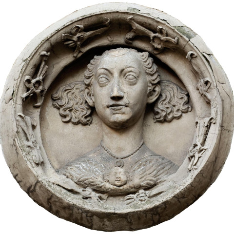 Ein rundes Steinrelief zeigt eine Person mit lockigem Haar, die ein detailliertes Gewand trägt, umgeben von einem dekorativen Rahmen. Der Ausdruck ist neutral und ruhig.