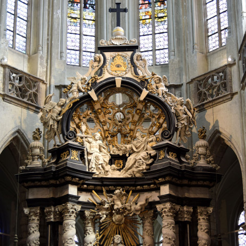 Prächtiger Kirchenaltar in einer Kathedrale, mit filigranen Skulpturen und Schnitzereien. Bunte Lichtstrahlen fallen durch die Oberlichter und erzeugen eine ehrfürchtige Atmosphäre.