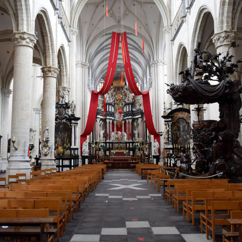 Das Bild zeigt ein prunkvolles Kircheninnere mit hohen Gewölbedecken, roten Bannern, Holzbänken und kunstvollen Schnitzereien und vermittelt eine feierliche, ehrfürchtige Atmosphäre.
