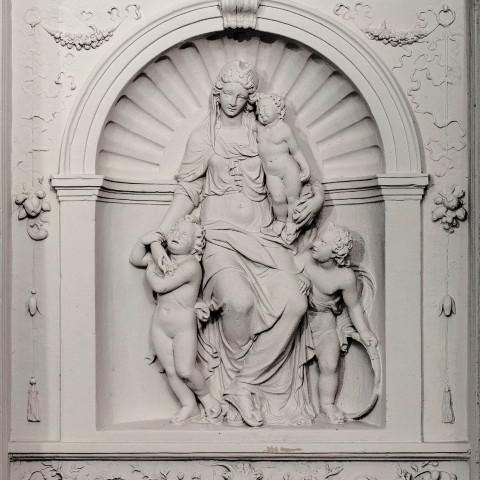 Aufwendiges Relief einer sitzenden Frau mit zwei Cherubinen, platziert in einer gewölbten Nische. Die detaillierte Blumen- und Bandverzierung verleiht Eleganz.