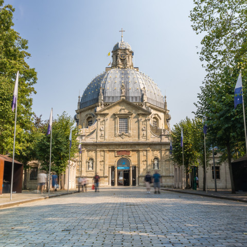 Ein Kuppelgebäude mit klassischer Architektur steht am Ende eines Kopfsteinpflasterwegs, umgeben von üppigen Bäumen, unter einem klaren blauen Himmel.